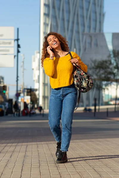 幸せな若いラテン語の女性の完全な体の肖像画歩くと街の外の携帯電話で話す — ストック写真