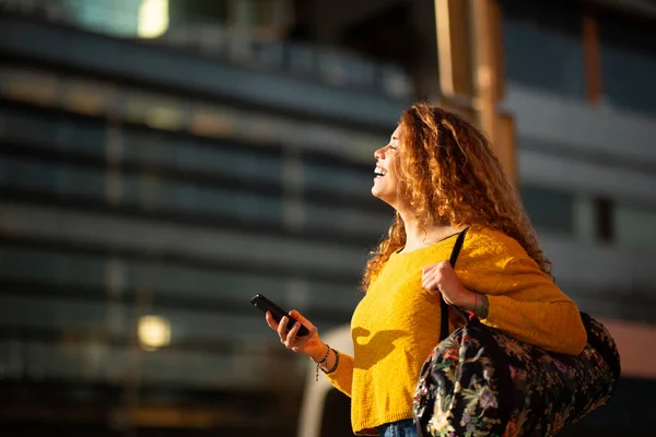笑顔若いラテン語の女性の横の肖像画袋と携帯電話で街の外を歩く — ストック写真