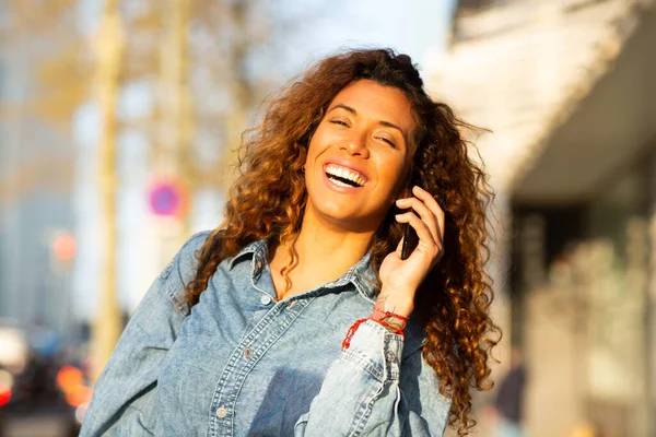 在城市里 一个笑着用手机在户外散步的年轻女子的近照 — 图库照片