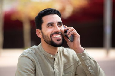 Dışarıda cep telefonuyla konuşan gülümseyen genç Arap 'ın portresini yakından çek.