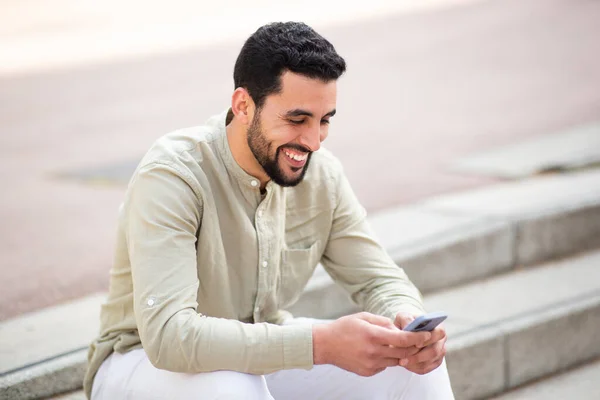 陽気な若い中東の男の肖像画は 階段の外に座って 携帯電話を使用して — ストック写真