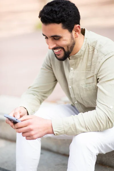 坐在外面用手机的快乐的阿拉伯年轻人的侧面肖像 — 图库照片