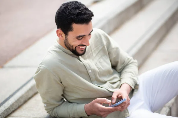 Portrét Veselého Mladého Araba Sedícího Venku Schodech Používajícího Mobilní Telefon — Stock fotografie