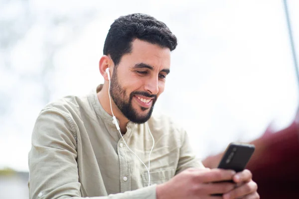 笑顔の北アフリカの男の肖像とともに外に座ってイヤホンから音楽を聴く携帯電話 — ストック写真