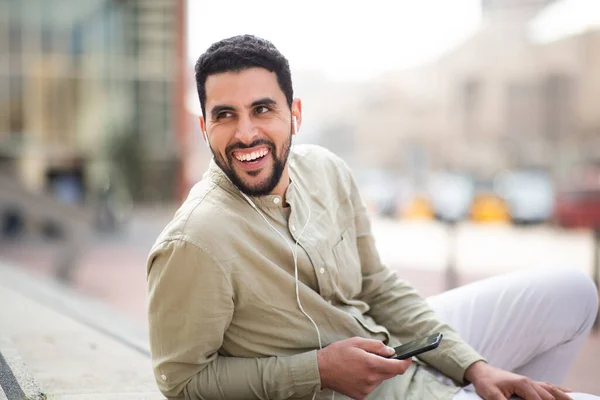 一个快乐的阿拉伯年轻人坐在外面用手机听音乐的画像 — 图库照片