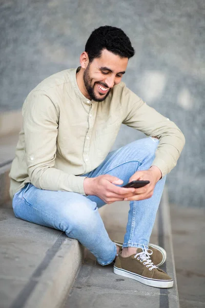 Портрет Веселого Молодого Человека Ближнего Востока Сидящего Ступеньках Пользующегося Мобильным — стоковое фото