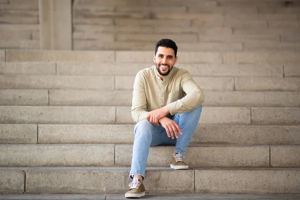 Yakışıklı Genç Arap Adamın Uzun Bir Portresi Merdivenlerde Oturuyor Kameraya — Stok fotoğraf