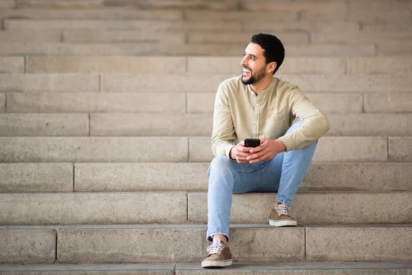 Портрет Молодого Араба Сидящего Ступеньках Мобильным Телефоном Смотрящего Сторону Улыбающегося — стоковое фото