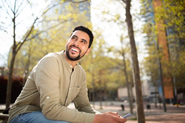 一个带着手机坐在外面笑的阿拉伯年轻人的画像 — 图库照片
