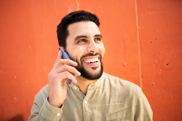 明るく若いですアラビア語の男の密接な肖像画で携帯電話で話しているオレンジの壁に対して離れて見て笑顔 — ストック写真