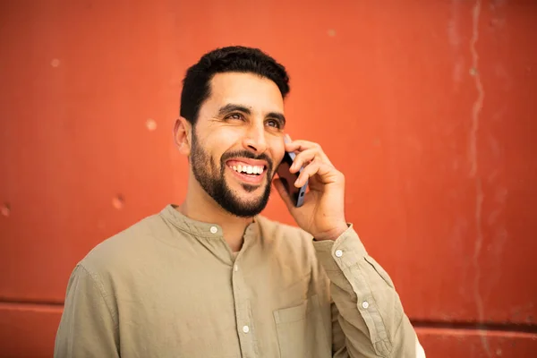 年轻英俊的阿拉伯男子靠在橙色墙上电话交谈的特写 — 图库照片