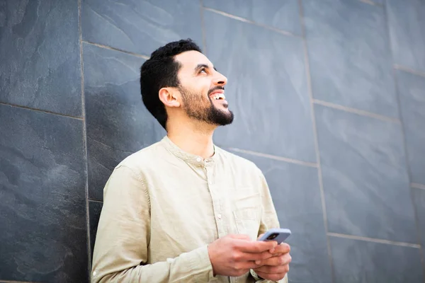一个快乐的阿拉伯年轻人的画像 他拿着手机靠在墙上朝外看 面带微笑 — 图库照片