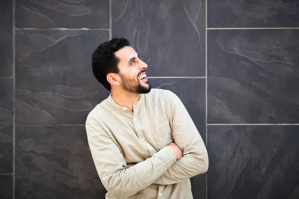 年轻的阿拉伯男子的画像 两臂交叉 靠着黑墙 望着别处笑着 — 图库照片
