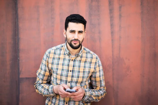 Portrét Mladého Araba Stojícího Mobilním Telefonem Hnědé Stěny — Stock fotografie
