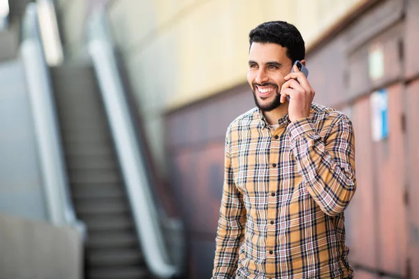 一个面带微笑的阿拉伯年轻人走在外面用手机说话的画像 — 图库照片