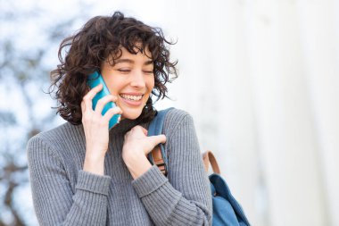 Dışarıda cep telefonuyla konuşan neşeli genç bir kadının yakın plan portresi.