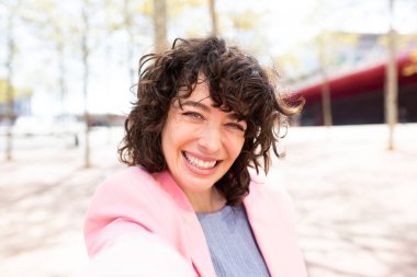 Şehrin dışında selfie çeken neşeli genç bir kadının yakın çekimi.