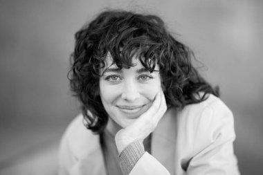 Elleri çenesinde kameraya bakan çekici bir genç kadının siyah beyaz portresini kapat.