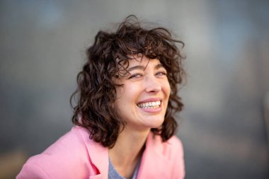 Genç beyaz kadın portresi kameraya bakıyor ve neşeyle gülümsüyor.