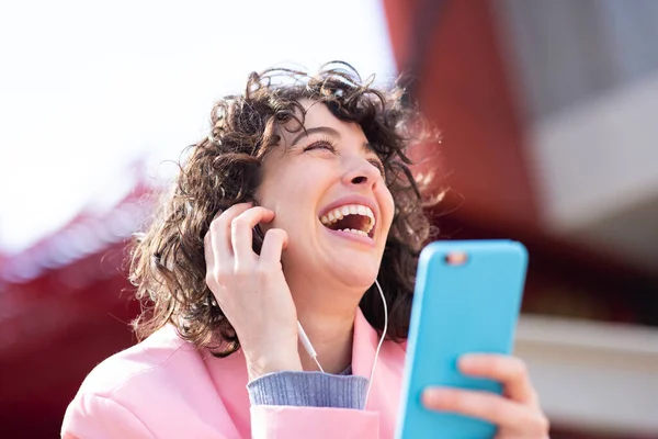 Portret Śmiejącej Się Kobiety Siedzącej Zewnątrz Słuchającej Muzyki Słuchawkami Telefonem — Zdjęcie stockowe
