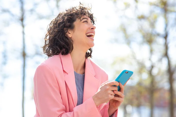 Portret Wesołej Młodej Kobiety Telefonem Odwracając Wzrok Śmiejąc Się Zewnątrz — Zdjęcie stockowe