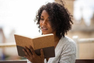 Açık havada kitap okuyan Afrikalı Amerikalı genç bir kadının portresi.