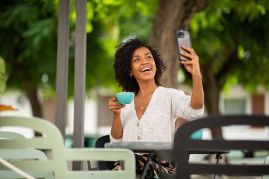 Portre Haopy Afro-Amerikalı kadın elinde kahve ve cep telefonuyla selfie çekiyor.