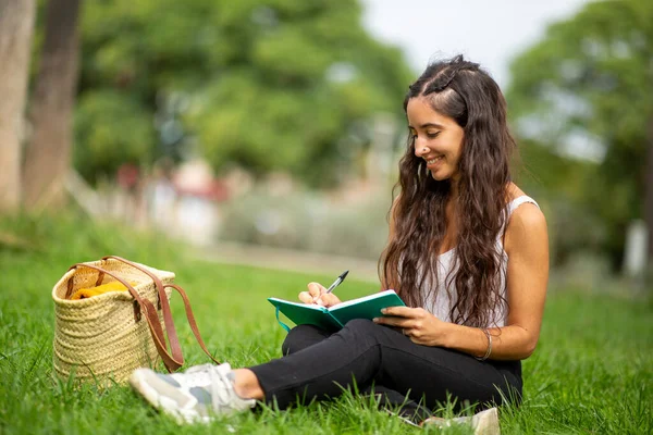 Parkta kitap yazan gülümseyen genç bir kadının portresi.