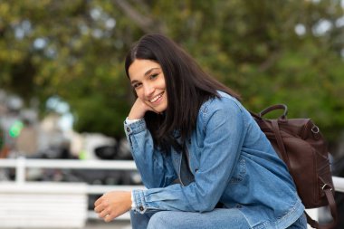 Açık havada oturan gülümseyen genç bir kadın.