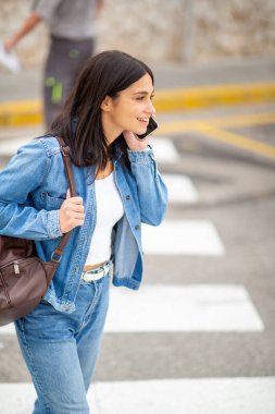 Cep telefonu ve çantasıyla yürüyen genç bir kadın.