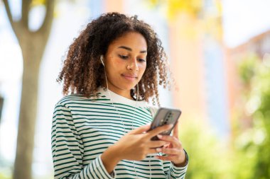 Akıllı telefonlu genç bir kadının portresi kulaklıkla dinliyor.