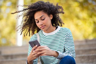 Portre genç Afrikalı Amerikalı kadın cep telefonuyla sohbet ediyor.