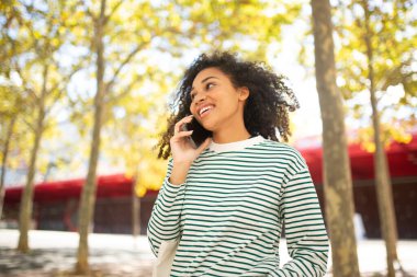 Gülümseyen genç Afrikalı Amerikalı kadın cep telefonuyla konuşuyor.