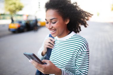 Sokakta cep telefonu ve çanta taşıyan genç bir kadın portresi.