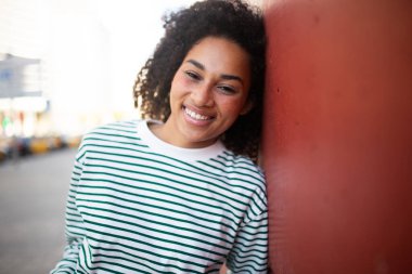 Duvara yaslanmış mutlu bir Afro-Amerikan kadını portresi.