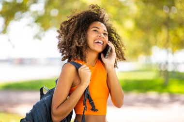 Çantalı mutlu kız öğrenci portresi cep telefonuyla konuşuyor.