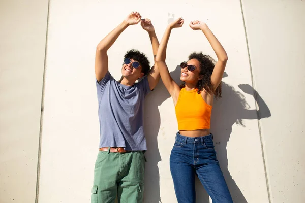 Portrait of happy couple with arms raised by white wall