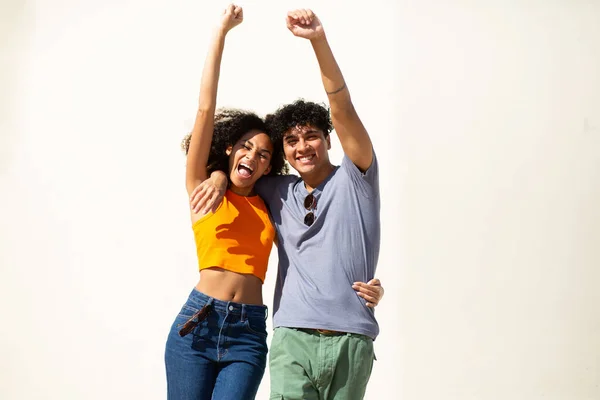 Portrait of cheerful young couple with arms raised by white background