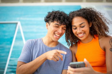 Birlikte cep telefonuna bakan gülümseyen genç adam ve kadının portresi.