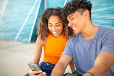 Birlikte cep telefonuna bakan genç bir çiftin portresi.