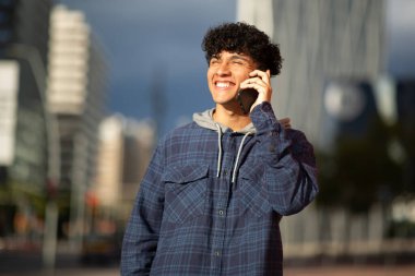 Şehirde cep telefonuyla konuşan gülümseyen genç adam portresi.