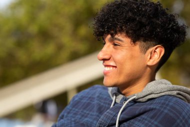 Yan portreyi kapat. Gülümse, kıvırcık saçlı, açık havada rahatlayan genç adam.