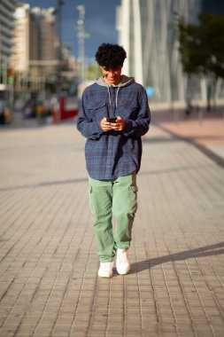 Tüm vücut portresi genç adam cep telefonuyla şehirde yürüyor.