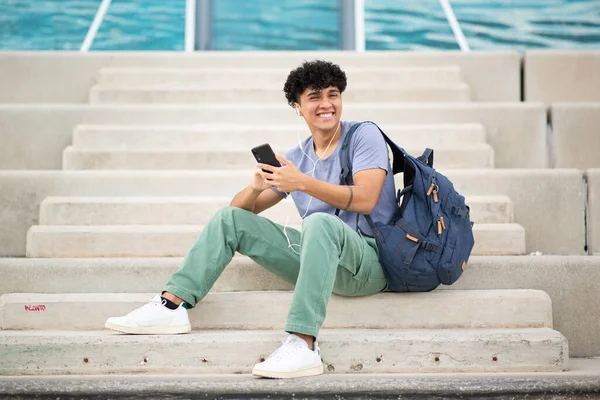 バッグと携帯でステップに座っている若い男を微笑む肖像画 — ストック写真