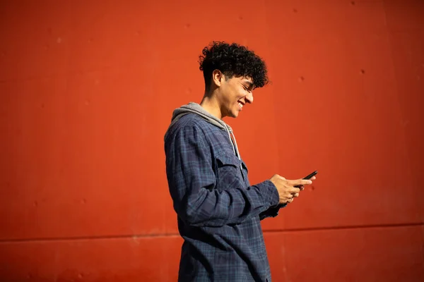 Foto Profil Tersenyum Anak Muda Dengan Ponsel Oleh Dinding Merah — Stok Foto