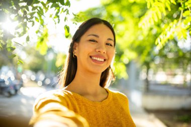 Parkta selfie çeken gülümseyen genç bir kadın.