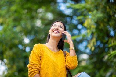 Parkta cep telefonuyla konuşan gülümseyen genç kadın portresi.