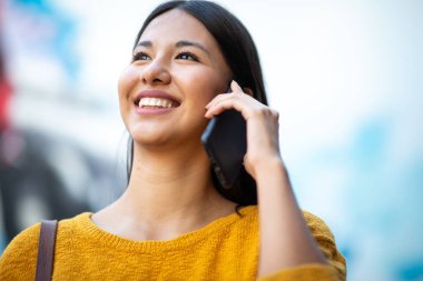 Kapalı alanda cep telefonuyla konuşan gülümseyen genç bir kadın.