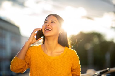 Dışarıda cep telefonuyla konuşan gülümseyen genç bir kadın portresi.