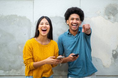 Cep telefonları ve parmakla işaret eden neşeli genç bir çift.